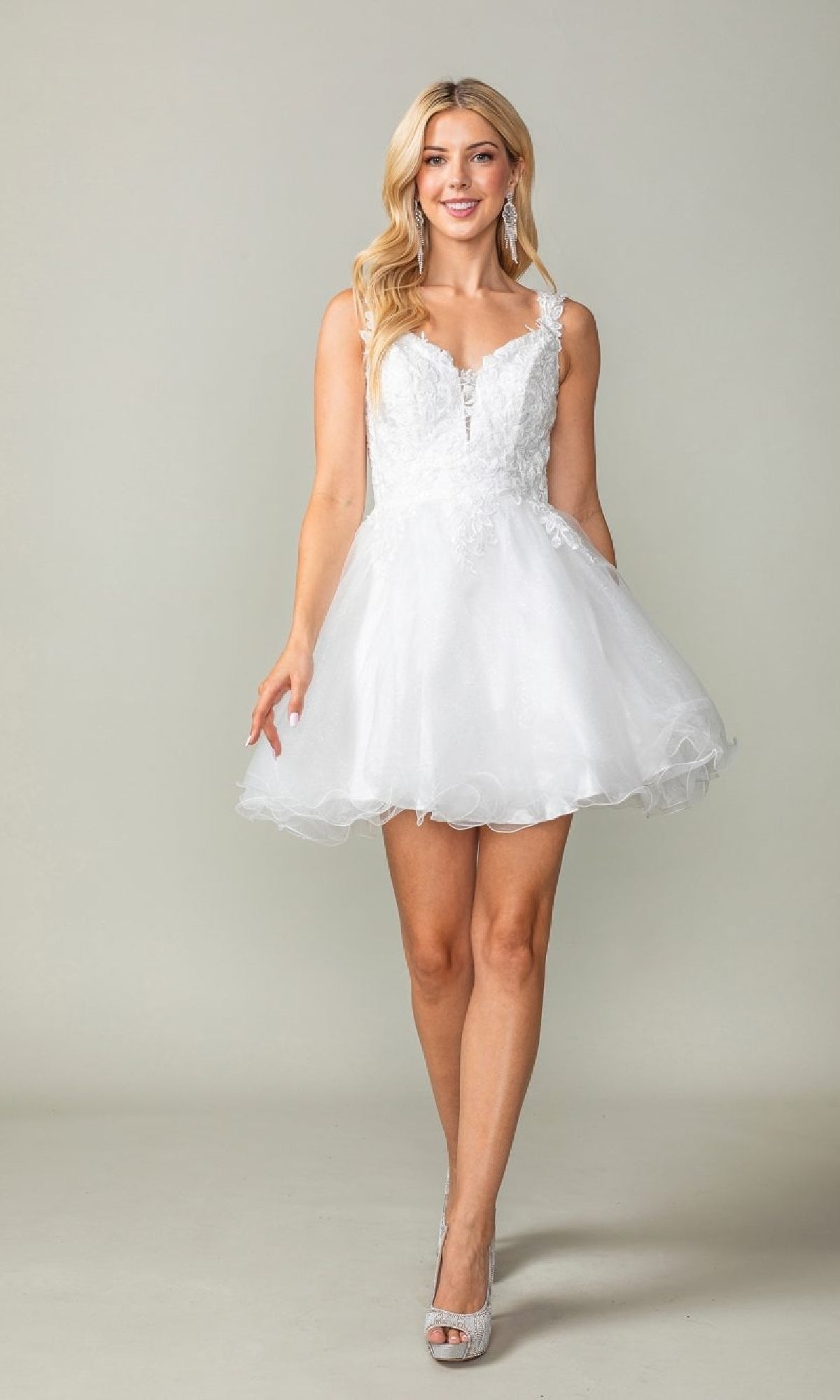 A woman models the Tulle Babydoll Homecoming Dress: Dancing Queen 3377, featuring a short white tulle flared skirt and peep-toe heels, posed against a plain light background.